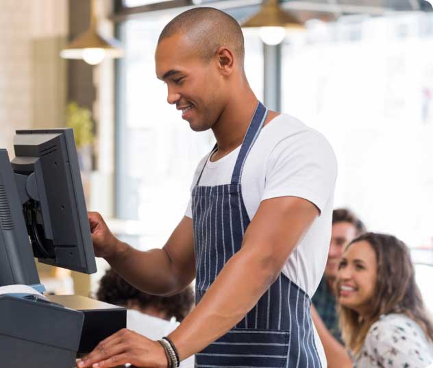 A retail worker using a countertop POS while customers wait